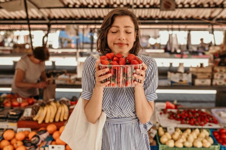 Portrait of a satisfied brunette holding fresh fruits just bought from an old lady market vendor.