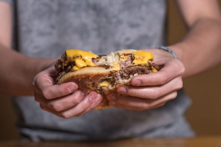 A closeup of a man cutting a cheeseburger by hand