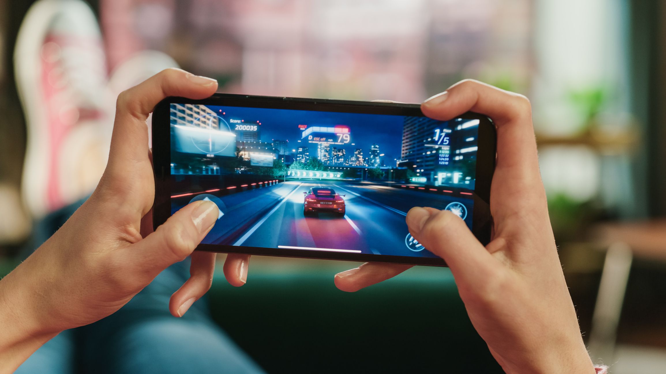 Female is Relaxing on a Couch at Home, Playing an Interactive Racing Drift Video Game on Her Smartphone. Gamer Lies on a Sofa in Living Room. Close Up POV Photo of Mobile Device Screen.