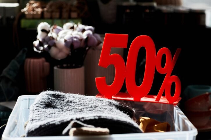 Close up of clothes bin in second hand store with 50 percent off red sale sign lit by sunlight