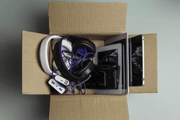 Cardboard box full of old used laptop computers, digital tablets, smartphones, power bank for recycling on gray background. Donation, e-waste, electronic waste for reuse, refurbish and recycle concept.