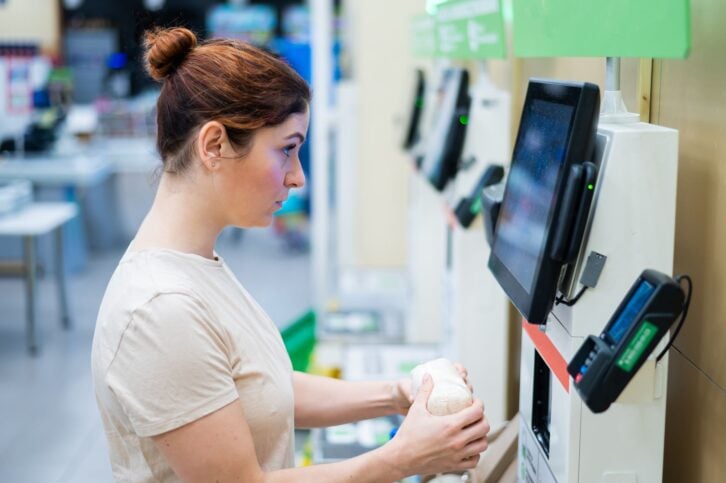 A frustrated woman uses a self-checkout counter. The girl does not understand how to independently buy groceries in the supermarket without a seller.