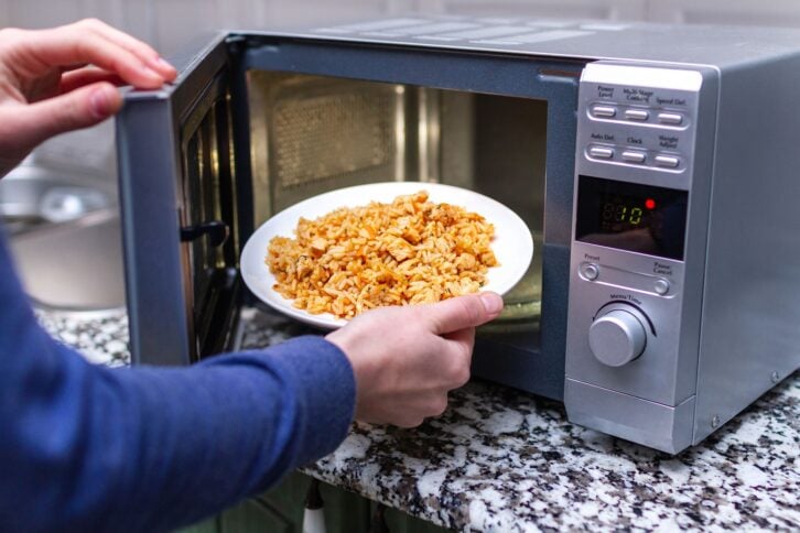 Using a microwave oven to warming up a plate of homemade pilaf for lunch at home. Hot meal