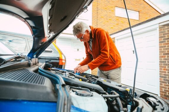 Color image depicting a man checking and maintaining the engine of his car, making sure everything is in working order.