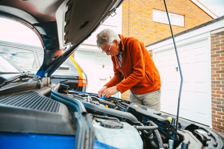 Color image depicting a man checking and maintaining the engine of his car, making sure everything is in working order.