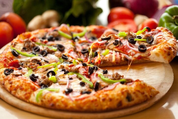 A slice of freshly baked supreme pizza, lifted from the entire pie.