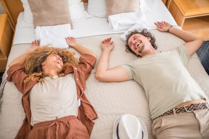A smiling loving couple lies in the bed of a hotel room, amazed by the comfort and beauty of the hotel accommodation