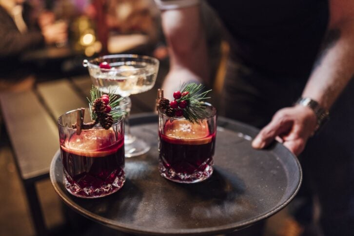 Close-up of a tray being held by an unrecognizable person. On the tray are Christmas themed cocktails