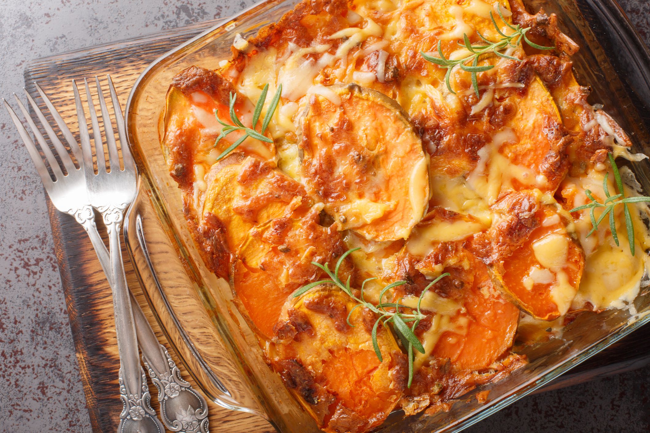 Homemade sweet potato gratin with cheddar cheese, eggs and rosemary close-up in a glass form on the table. Horizontal top view from above