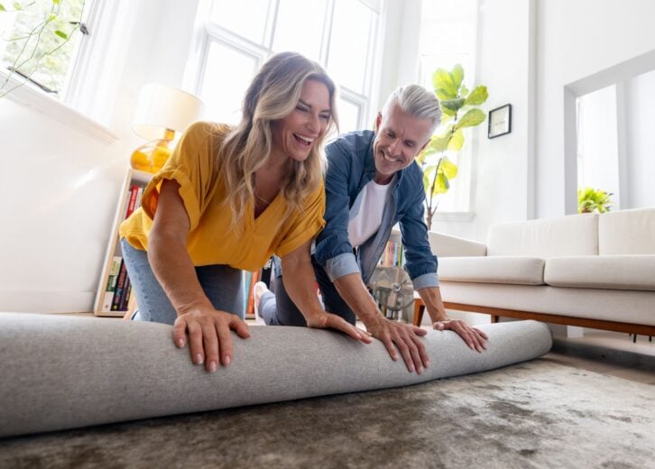 Happy loving couple moving house and unrolling a carpet while unpacking - domestic life concepts