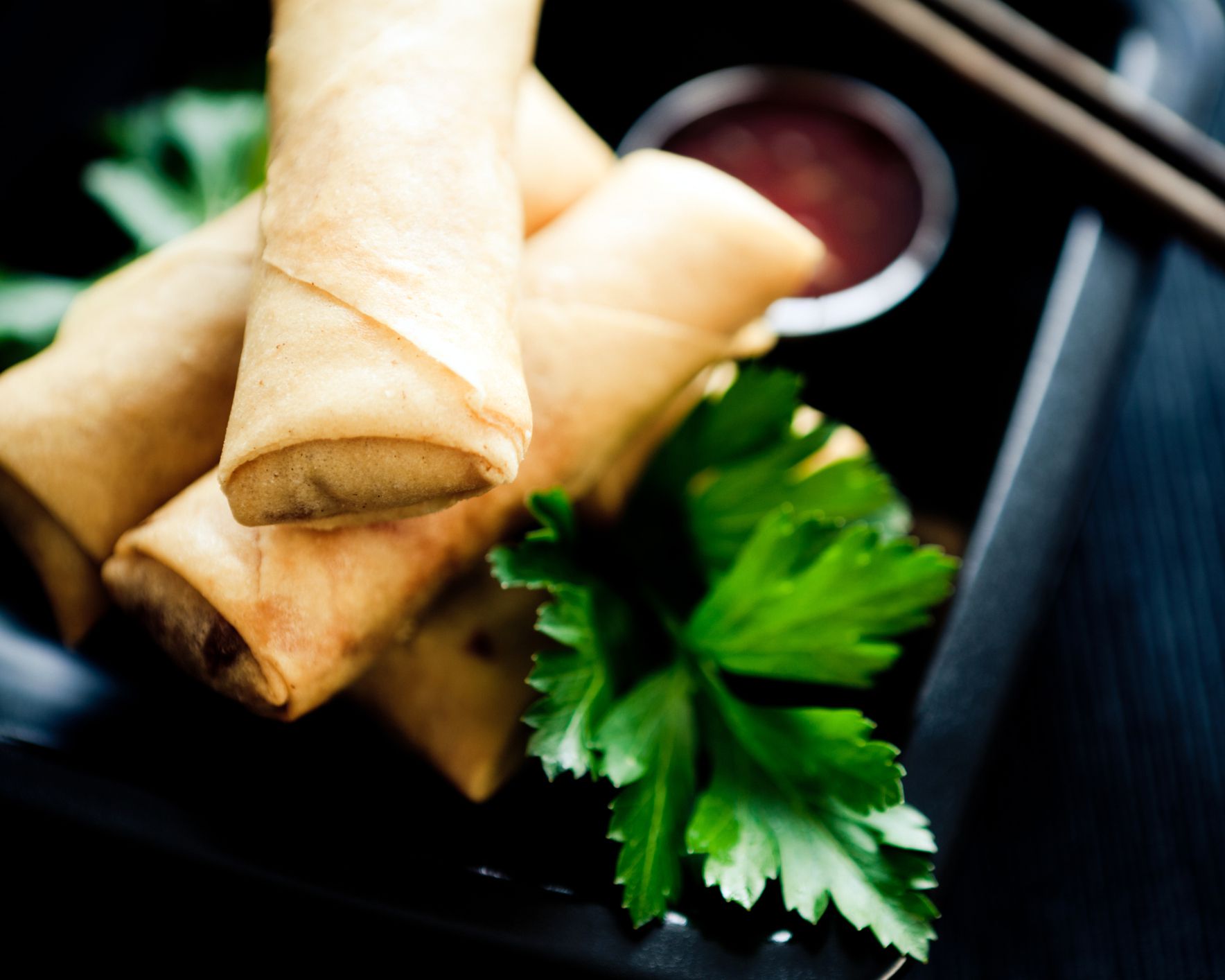 baked egg rolls with cilantro, red sauce and chopsticks in background