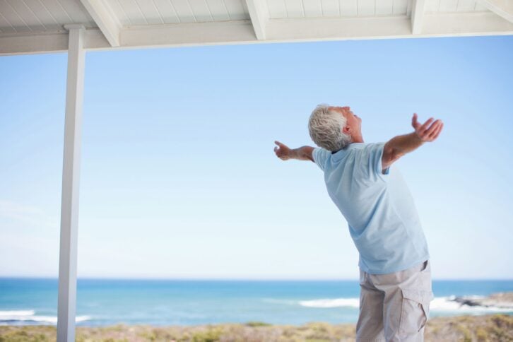 senior man standing with arms outstretched, ocean in background