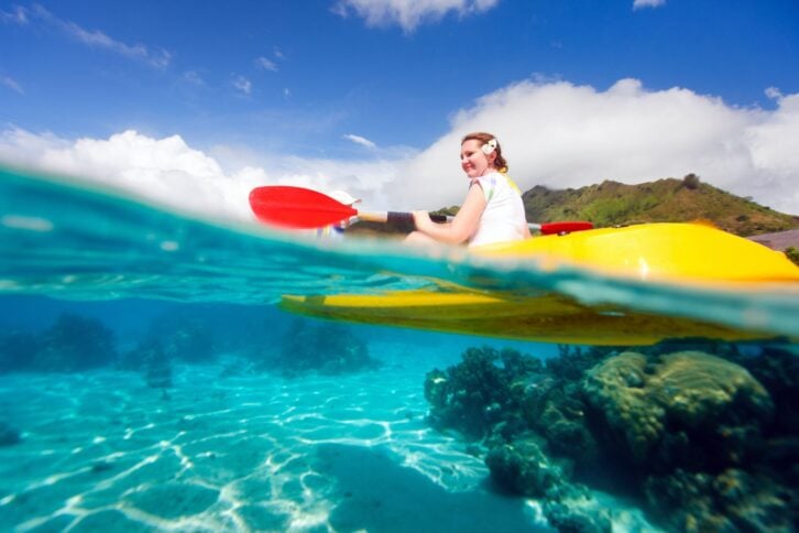 young woman kayaking over coral reef