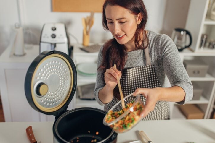 Hispanic woman using slow cooker while preparing food in the kitchen