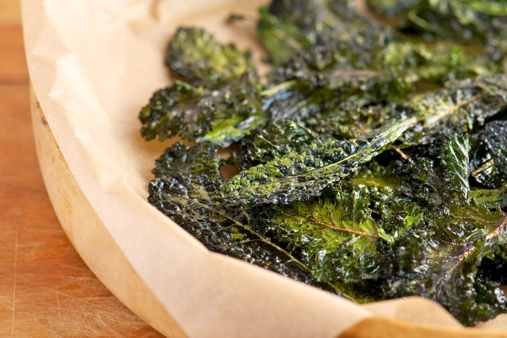 crispy kale chips in paper-lined bowl on wooden surface