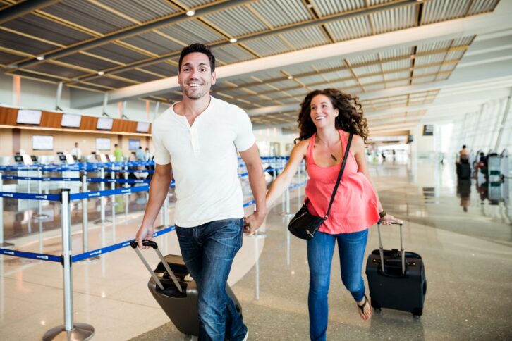 couple excited at the airport with suitcases, running to plane