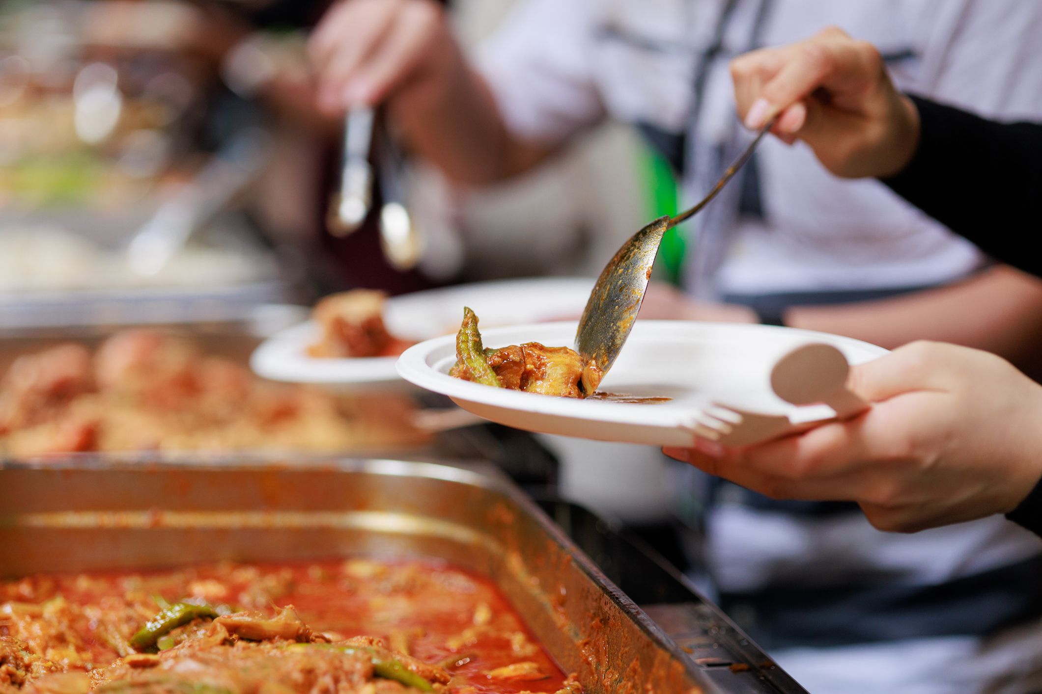 A cropped image captures business people using service tongs to carefully select their food from the buffet line, showcasing a refined and organized dining experience.