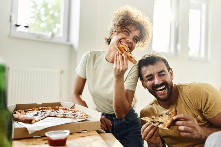 Cheerful couple having fun while eating pizza at their new renovating apartment. Copy space.