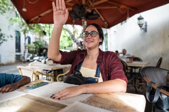 Young woman waving to waiter at the restaurant