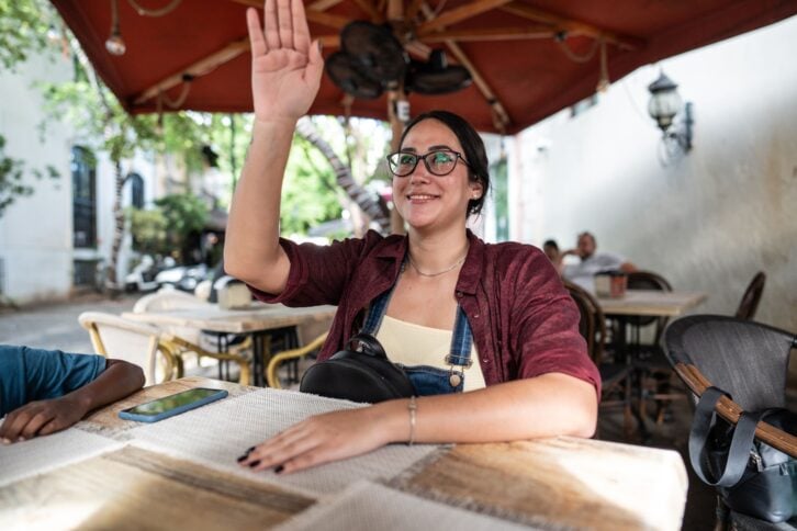 Young woman waving to waiter at the restaurant
