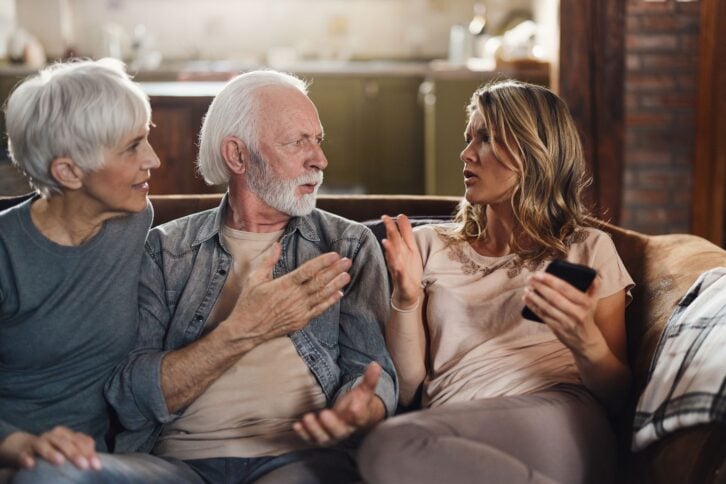 Senior parents feeling frustrated while their adult daughter is using smart phone at home.