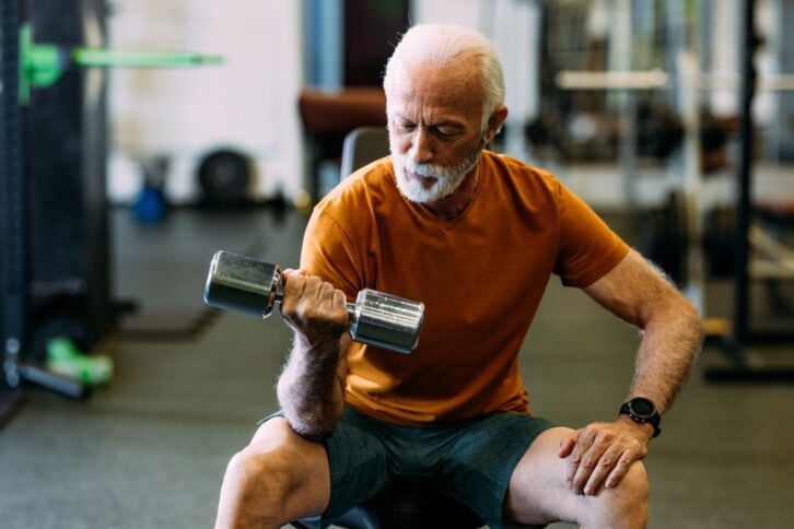 Elderly man lifting dumbbells in a gym setting, focusing on strength training and fitness. Promotes healthy aging and active lifestyle.
