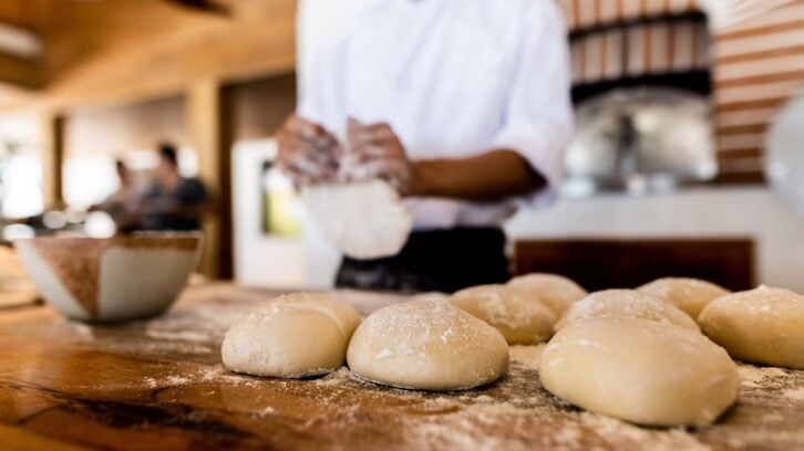 Black pizza baker chef preparing dough in front of pizza oven