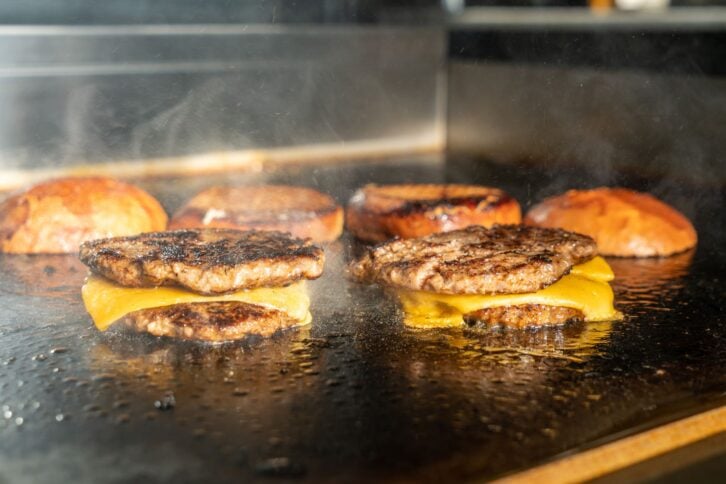 Make burgers on the grill restaurant. Burgers cooking on a gas grill, how to make a burger step by step. A person using a spatula to cut meat. a person cutting meat on a grill with a knife