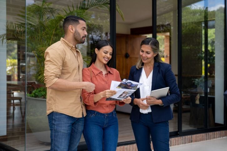 Couple talking to a real estate agent while looking at a house and checking some flyers - home ownership concepts