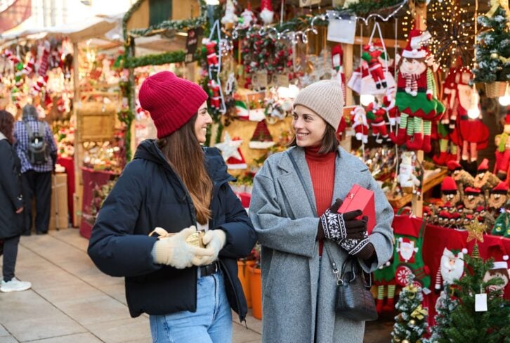 Two friends are holding gifts and enjoying the festive atmosphere of a traditional christmas market