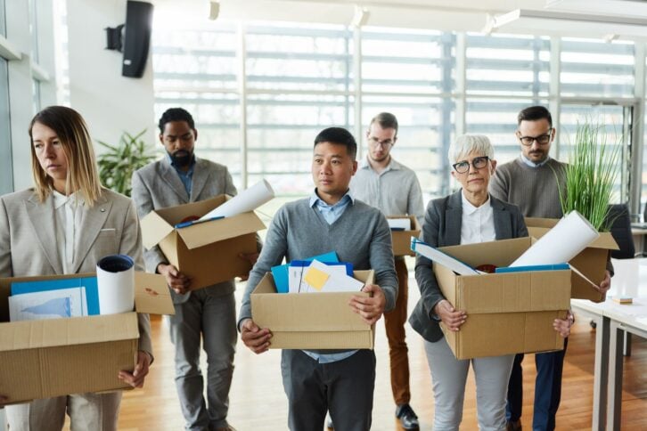Large group of displeased business people carrying carton boxed with their belongings after being fired from their jobs.