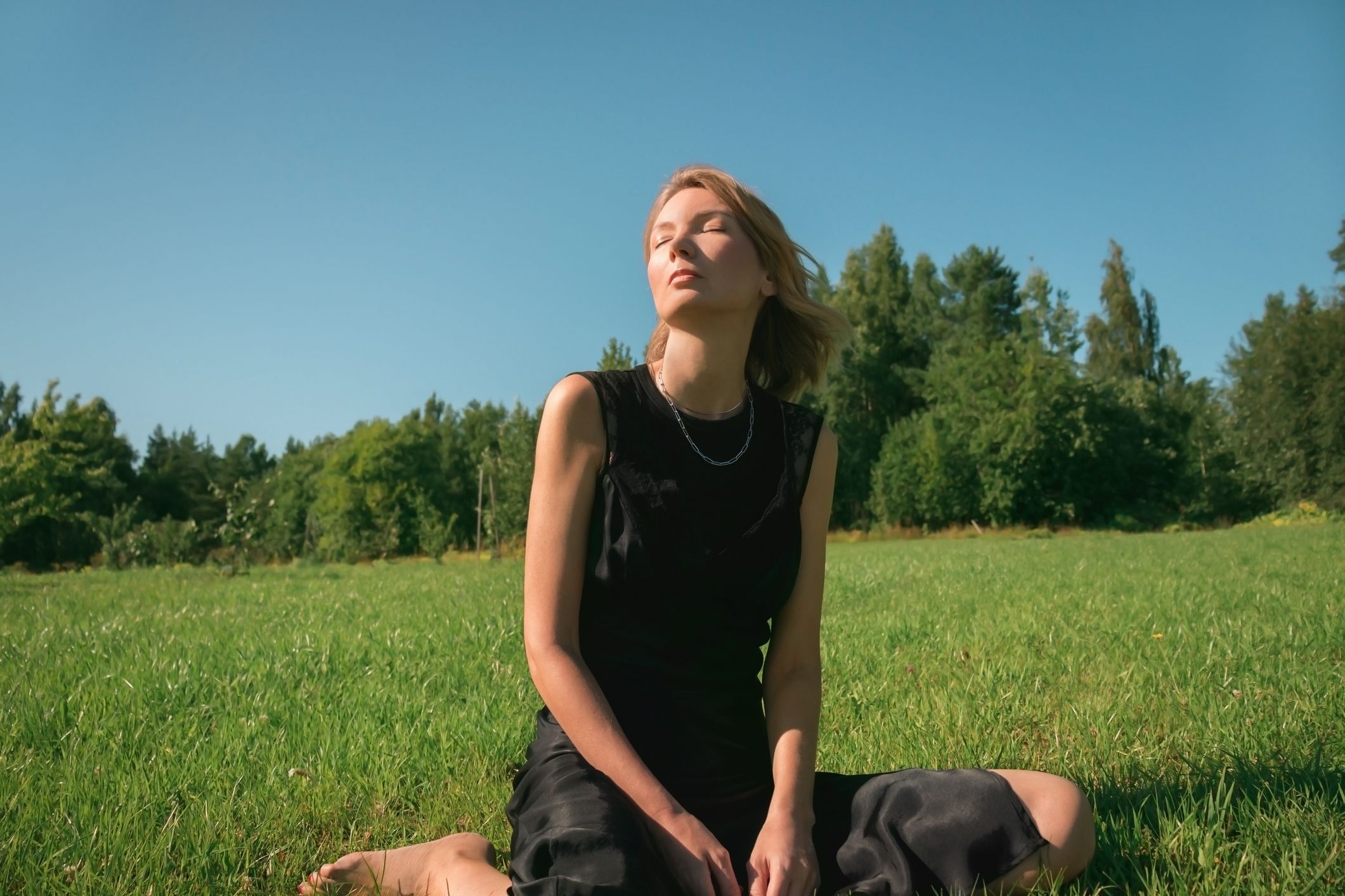 Young adult woman sitting on grass in park, summer sunny day.