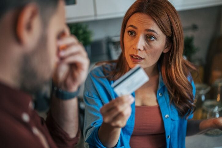 A husband and wife are arguing in the kitchen while holding a credit card.