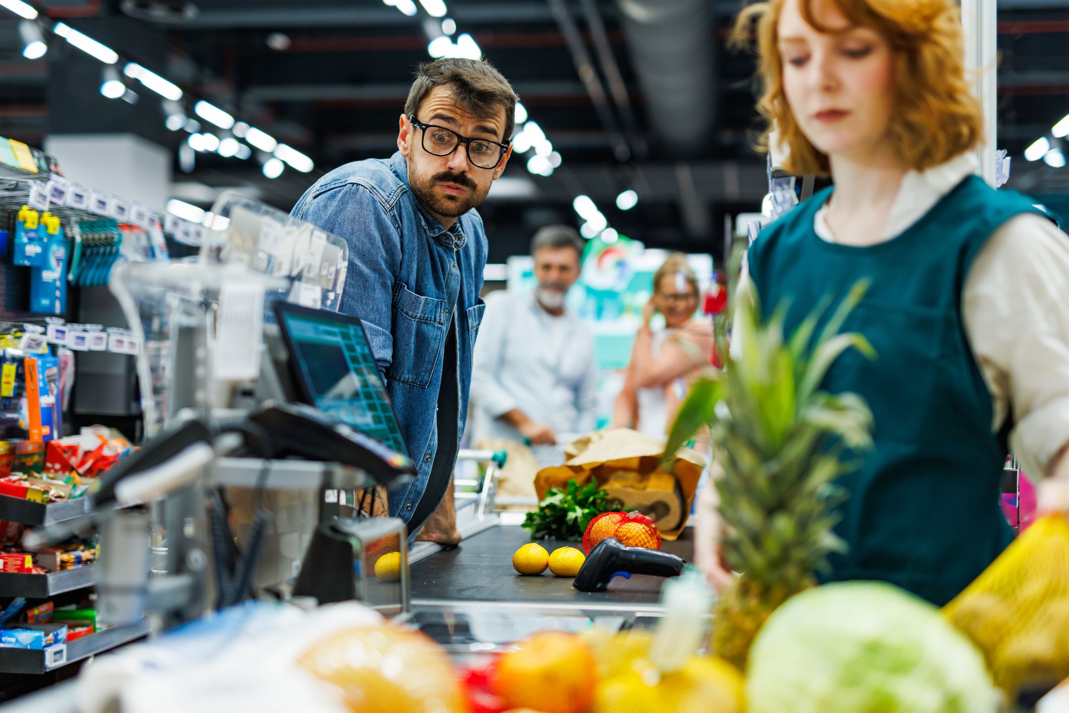 Curious customer is observing the groceries of another shopper while waiting in line at the supermarket checkout, creating a humorous and relatable scene of everyday life