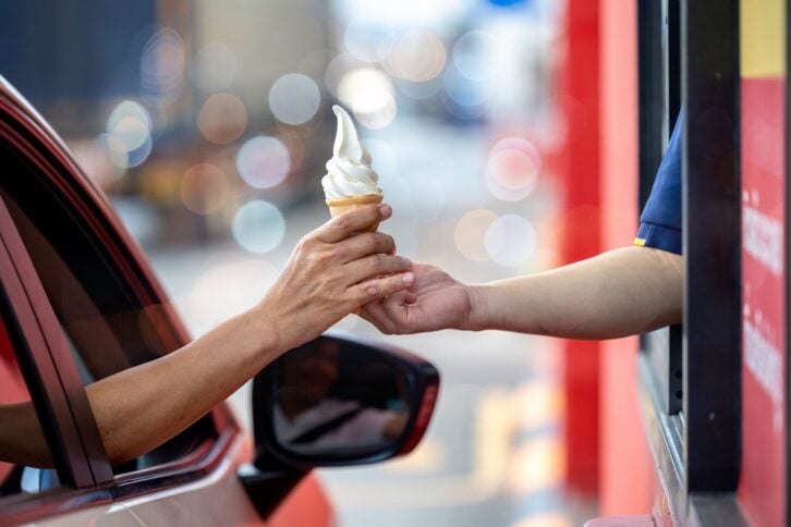 Hand Man in car receiving coffee in drive thru fast food restaurant. Staff serving takeaway order for driver in delivery window. Drive through and takeaway for buy fast food for protect covid19.