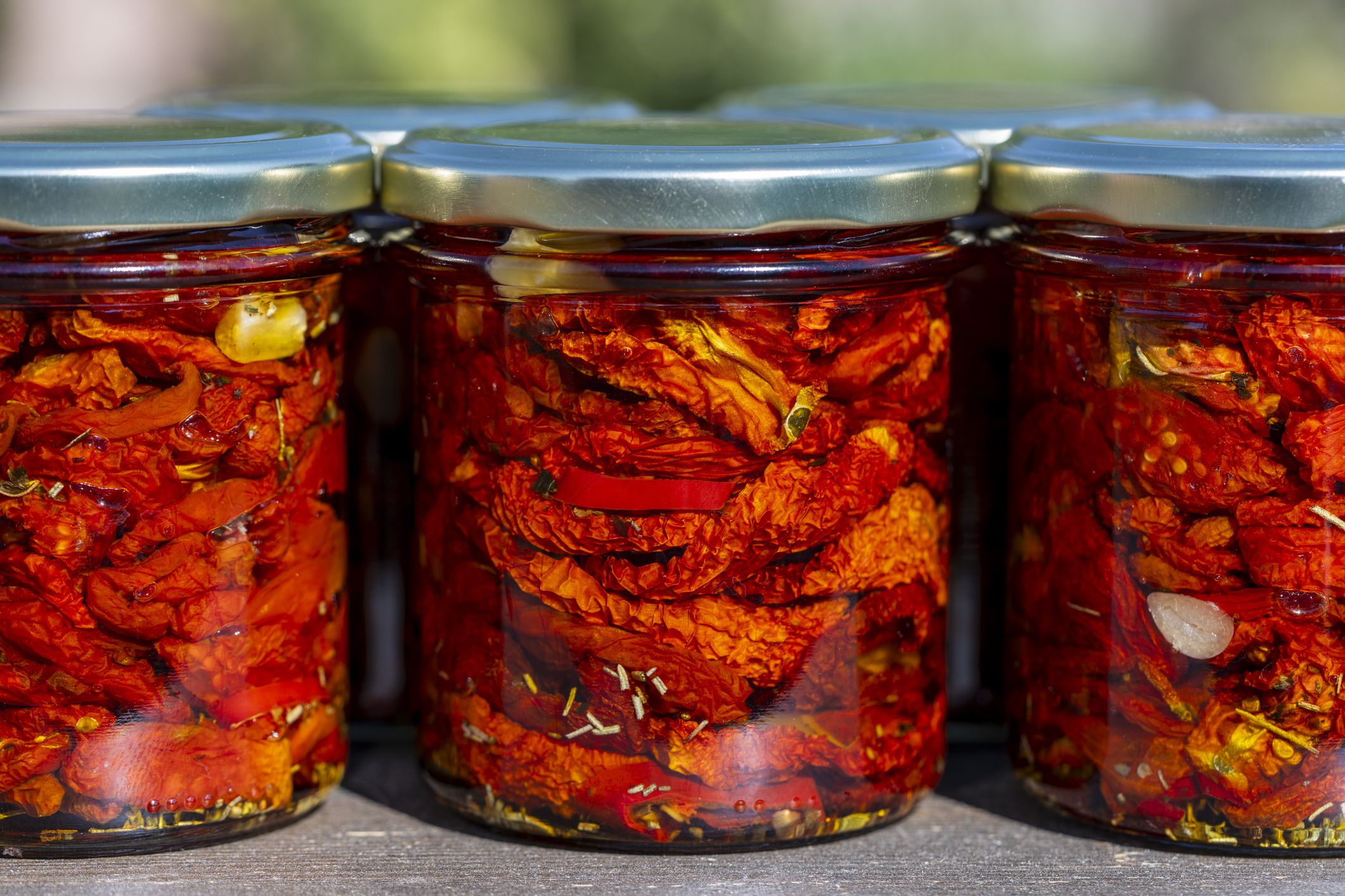 Sun-dried red tomato with garlic, rosemary, olive oil and spices in a glass jars on a wooden table. Rustic style, close up