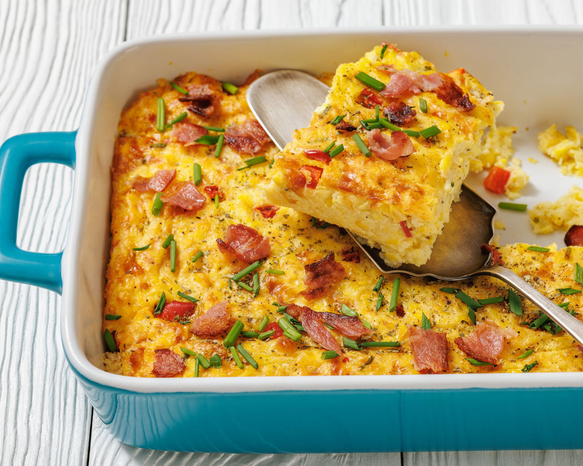 freshly baked corn pudding casserole sprinkled with chives and crispy fried bacon in a baking dish with cake shovel, horizontal view from above, close-up