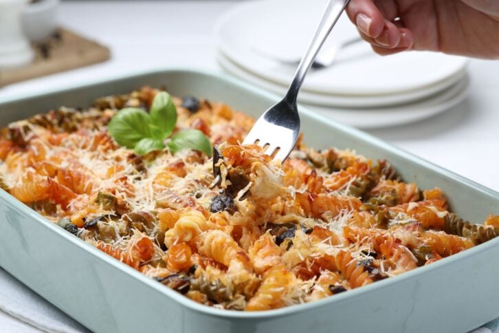 Woman eating delicious al forno pasta at white table, closeup