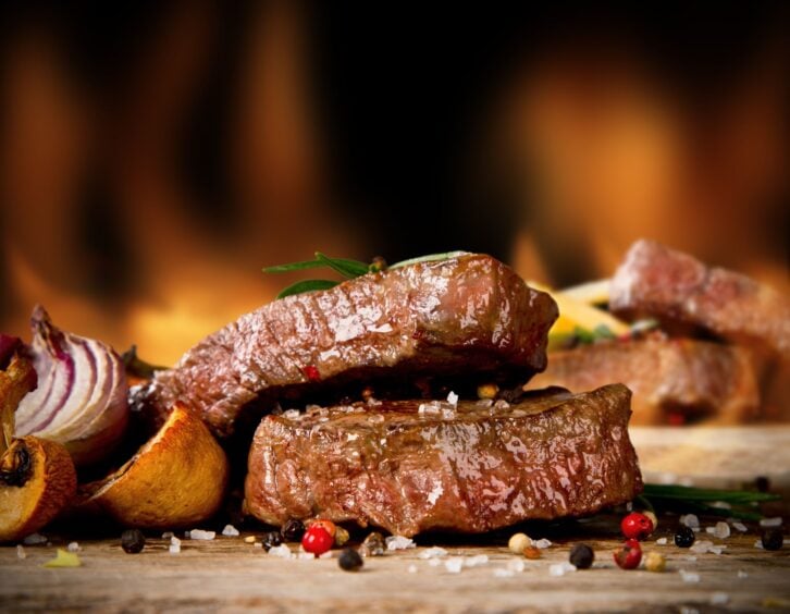 Delicious beef steaks with fire on background