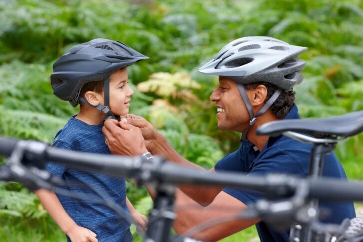 Caring father helping son put on bicycle helmet