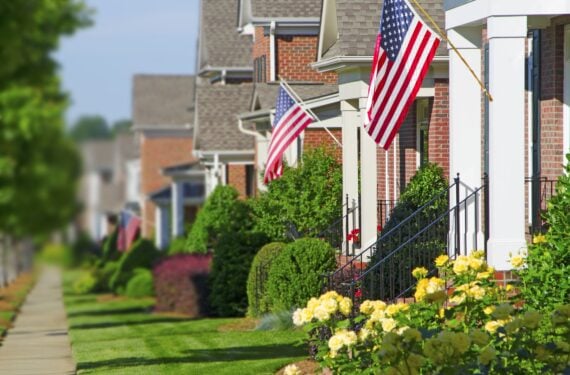 American Flags hang from the front porches of a row of upscale brick homes in celebration of the upcoming holiday.Taken in the Summer with beautiful late evening sunlight. Background is blurred to add emphasis on the flag in the foreground.