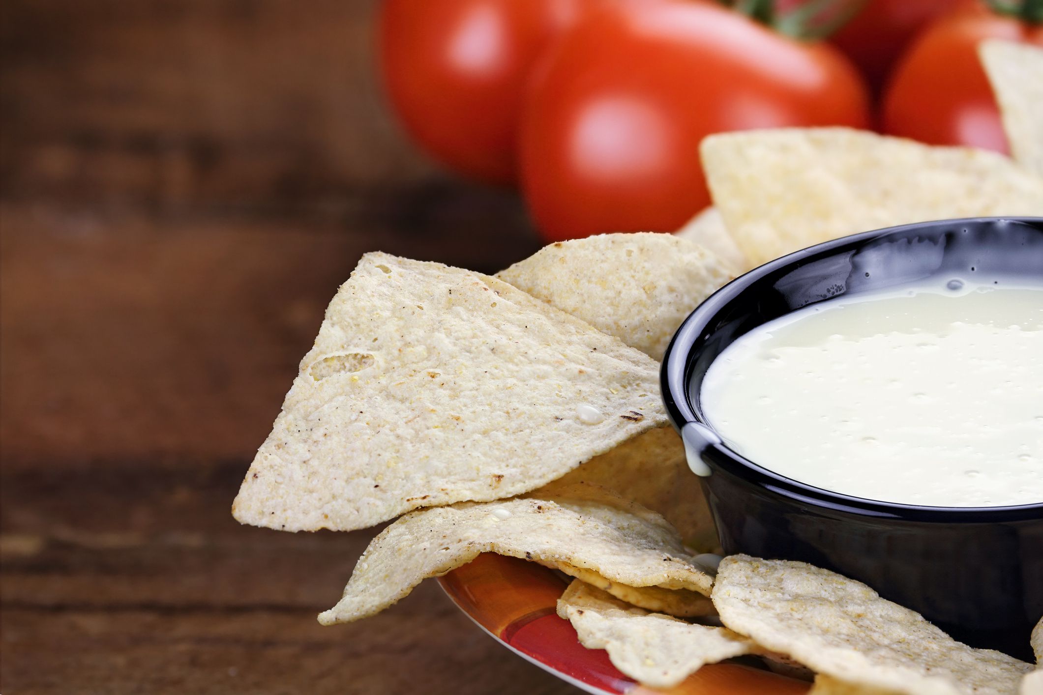 Queso Blanco or White Cheese Sauce with corn tortilla chips and fresh tomatoes. Extreme shallow depth of field with selective focus on cheese dip.