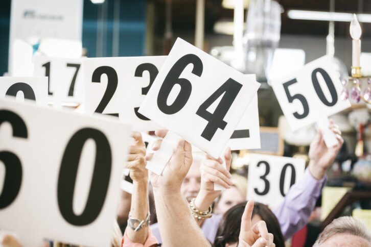 A crowd of bidders at an auction, holding their numbered bidding paddles in the air.
