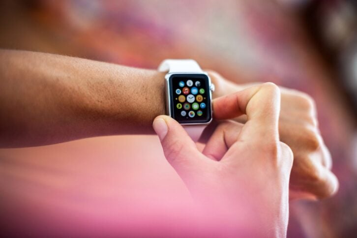 Apple Watch Sport model being worn on a girl's left wrist. This smartwatch has a 38 mm screen in a silver aluminium case with a white, soft plastic sports band.