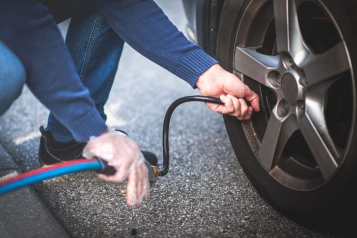 adult checking pressure and inflating car tire