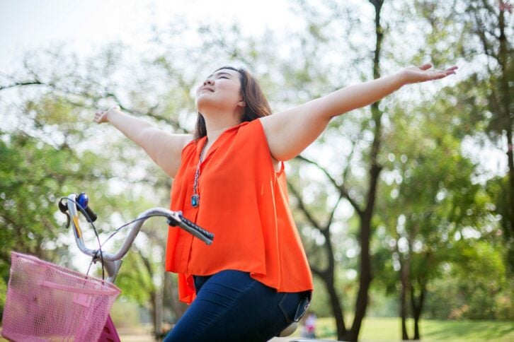 happy woman in bicycle with arms outstretched