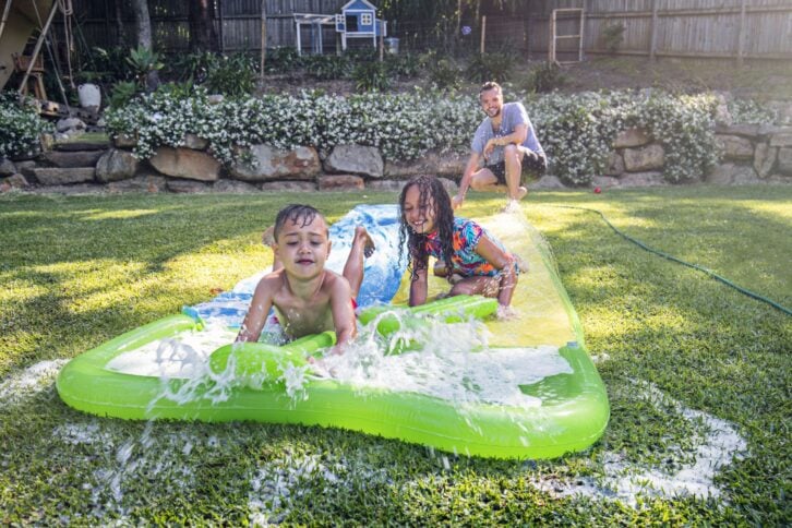 children having fun on the slip 'n slide in the back garden with their father