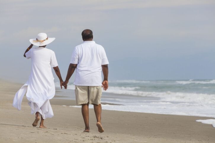 Happy romantic senior African American man and woman couple walking holding hands on a deserted tropical beach