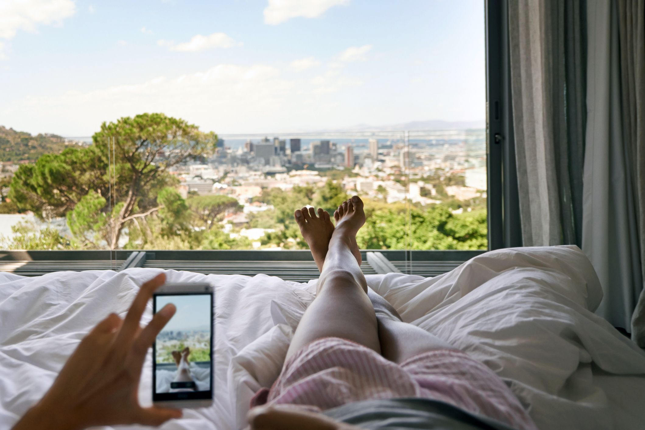 cropped shot of a woman in bed taking a picture of the view from her hotel room