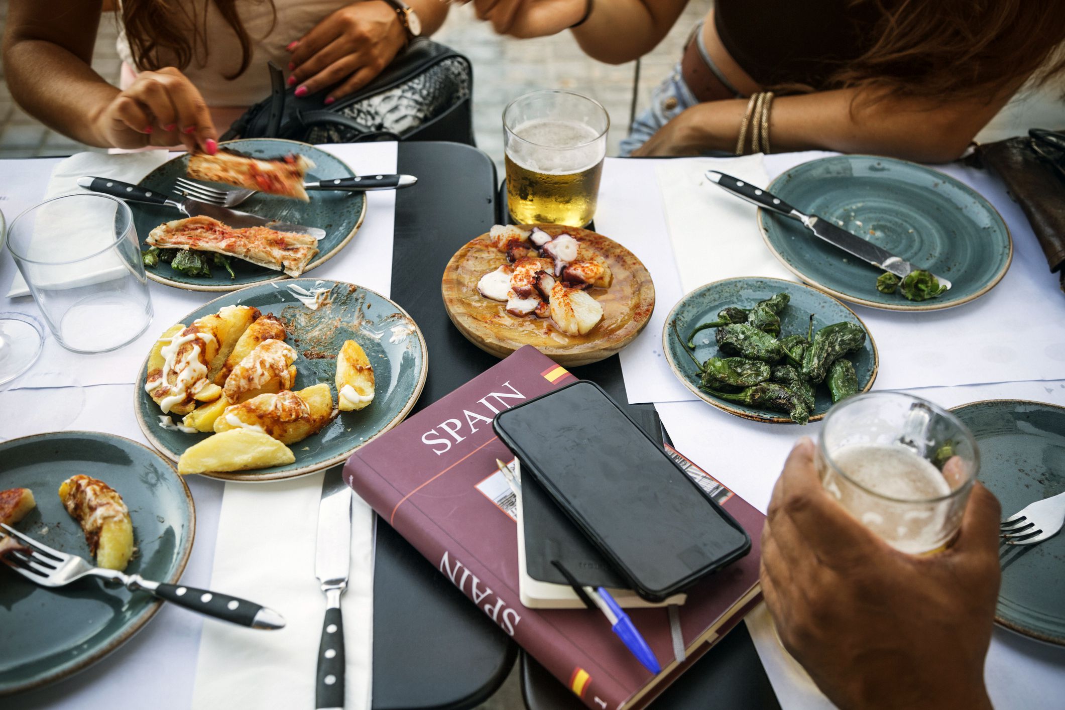 tourists in barcelona eating tapas in a typical restaurant in the barri gotic. on the table a travel guide of spain and a smartphone